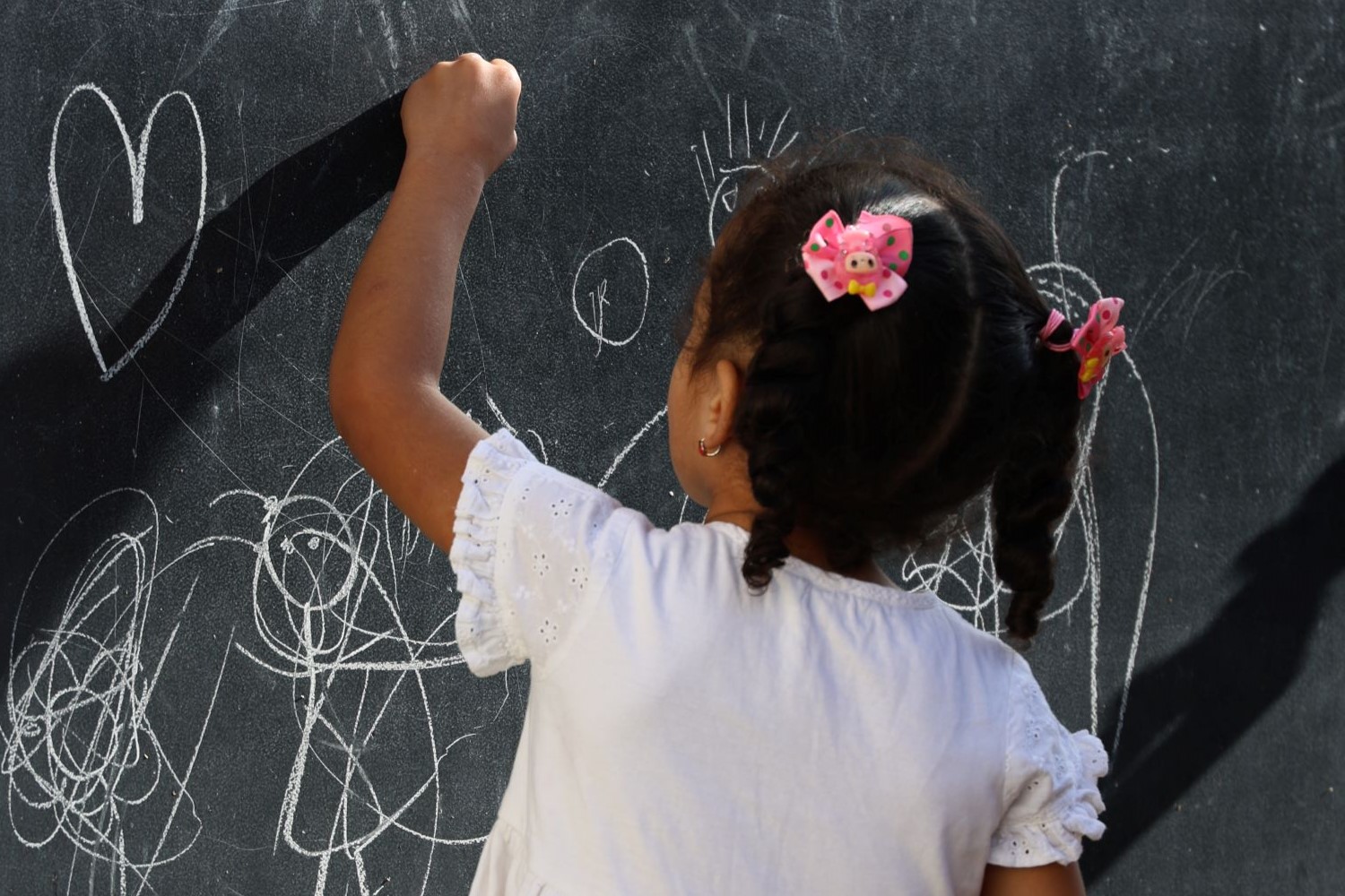 Une petite fille, de dos, dessine à la craie sur un tableau